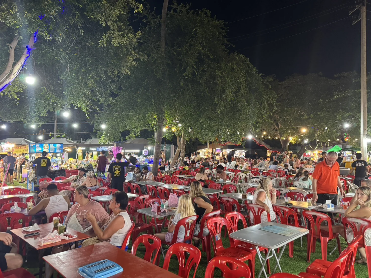 Bustling evening atmosphere at Fisherman's Village in Bophut, Koh Samui, with visitors dining outdoors beneath illuminated trees.