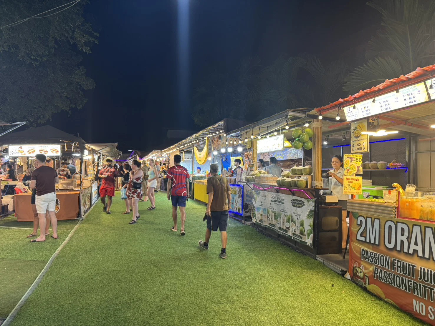 Tourists strolling past illuminated market stalls at Fisherman's Village Walking Street in Bophut, Koh Samui, at night.