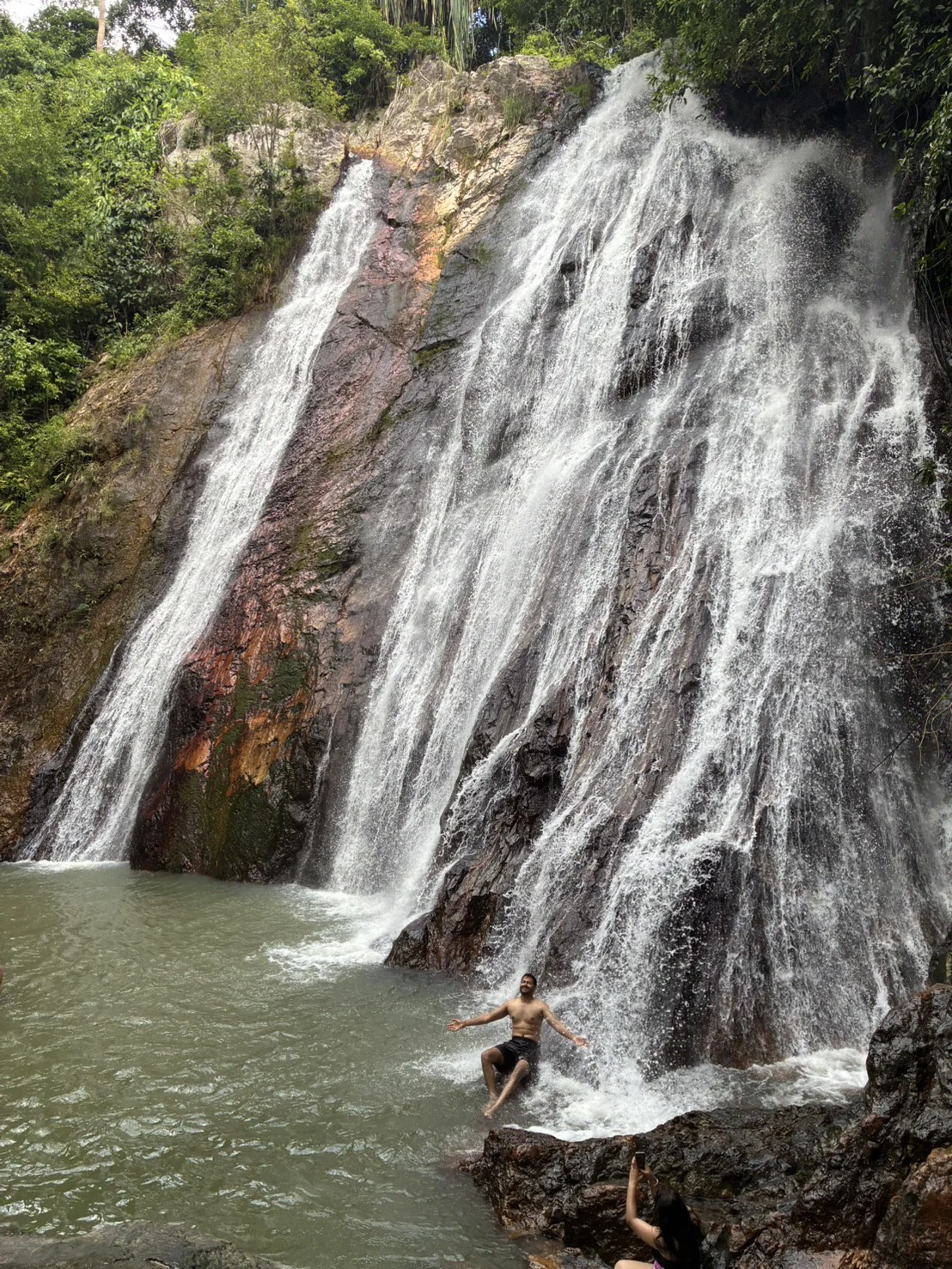 Water cascading down a large rocky cliff into a natural pool at a waterfall on Koh Samui, Thailand.
