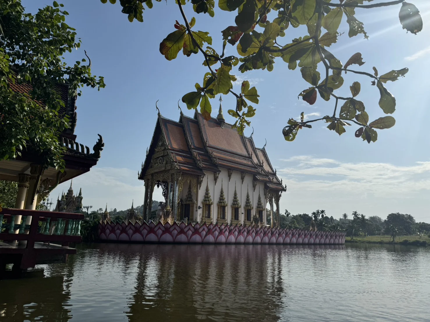 Traditional Thai Buddhist temple building beside a peaceful lake at Wat Plai Laem in Koh Samui, Thailand.